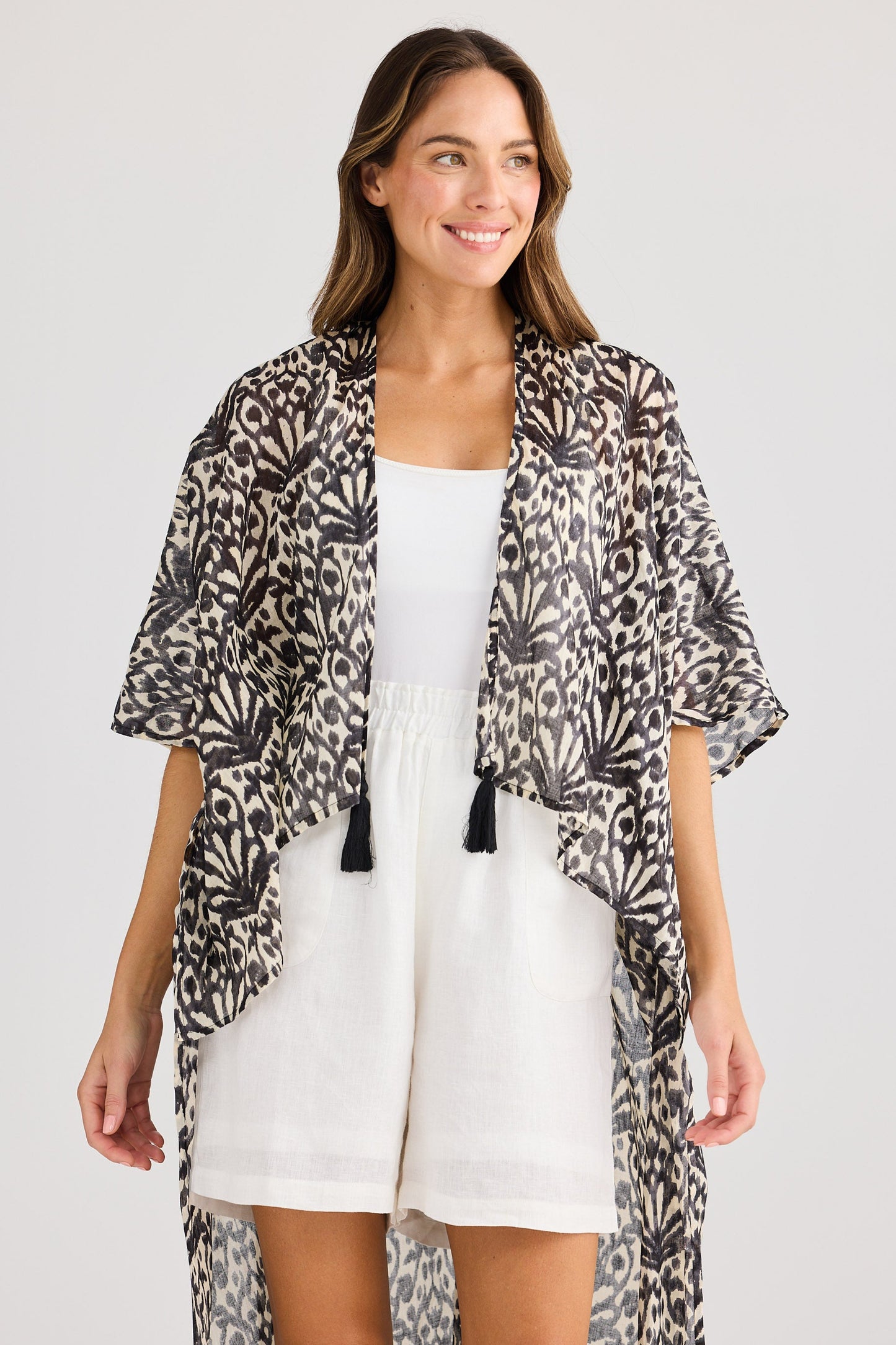 Woman wearing a leopard print kimono over a white dress on a plain background