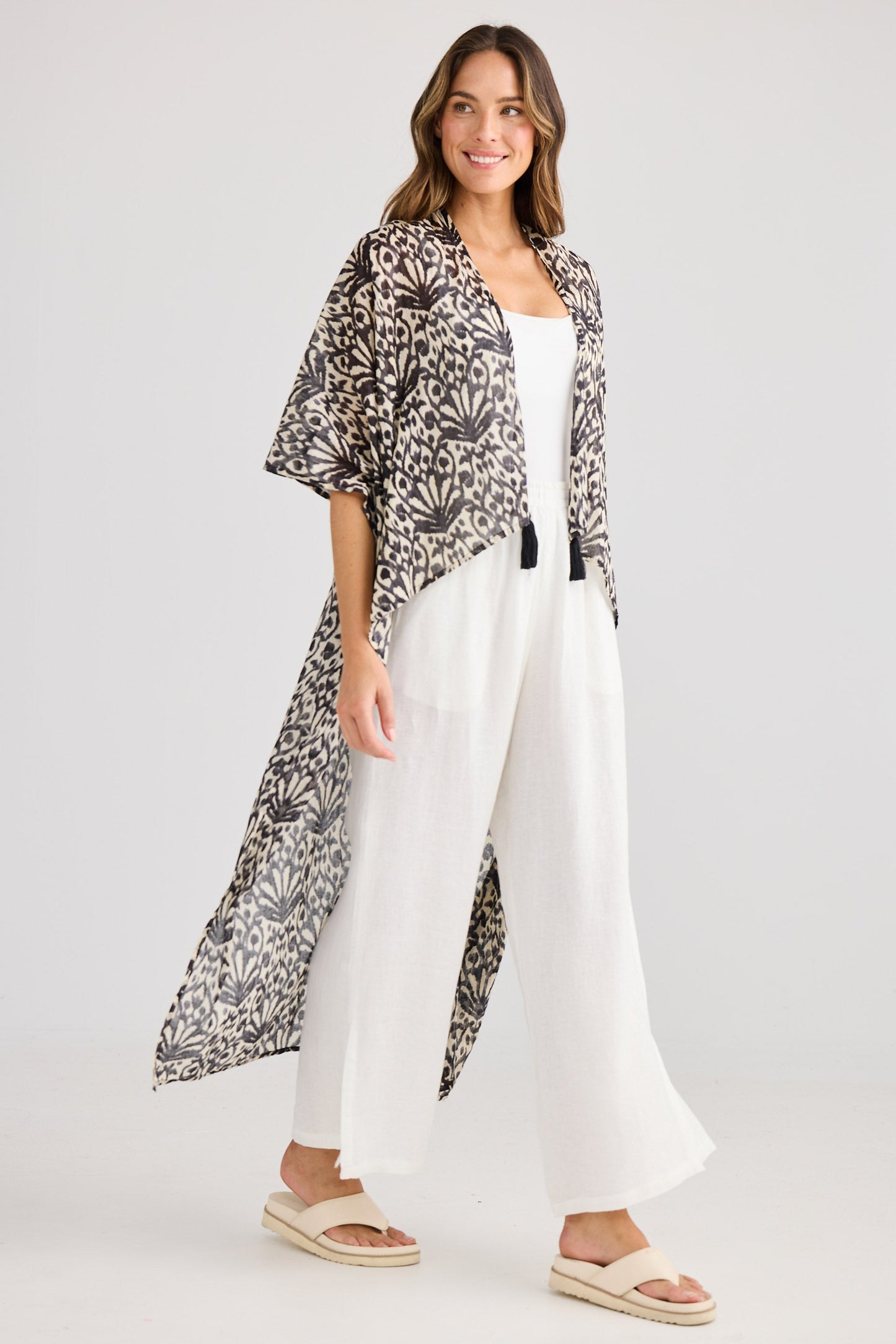 Woman wearing a patterned kimono-style jacket over a white outfit on a plain background