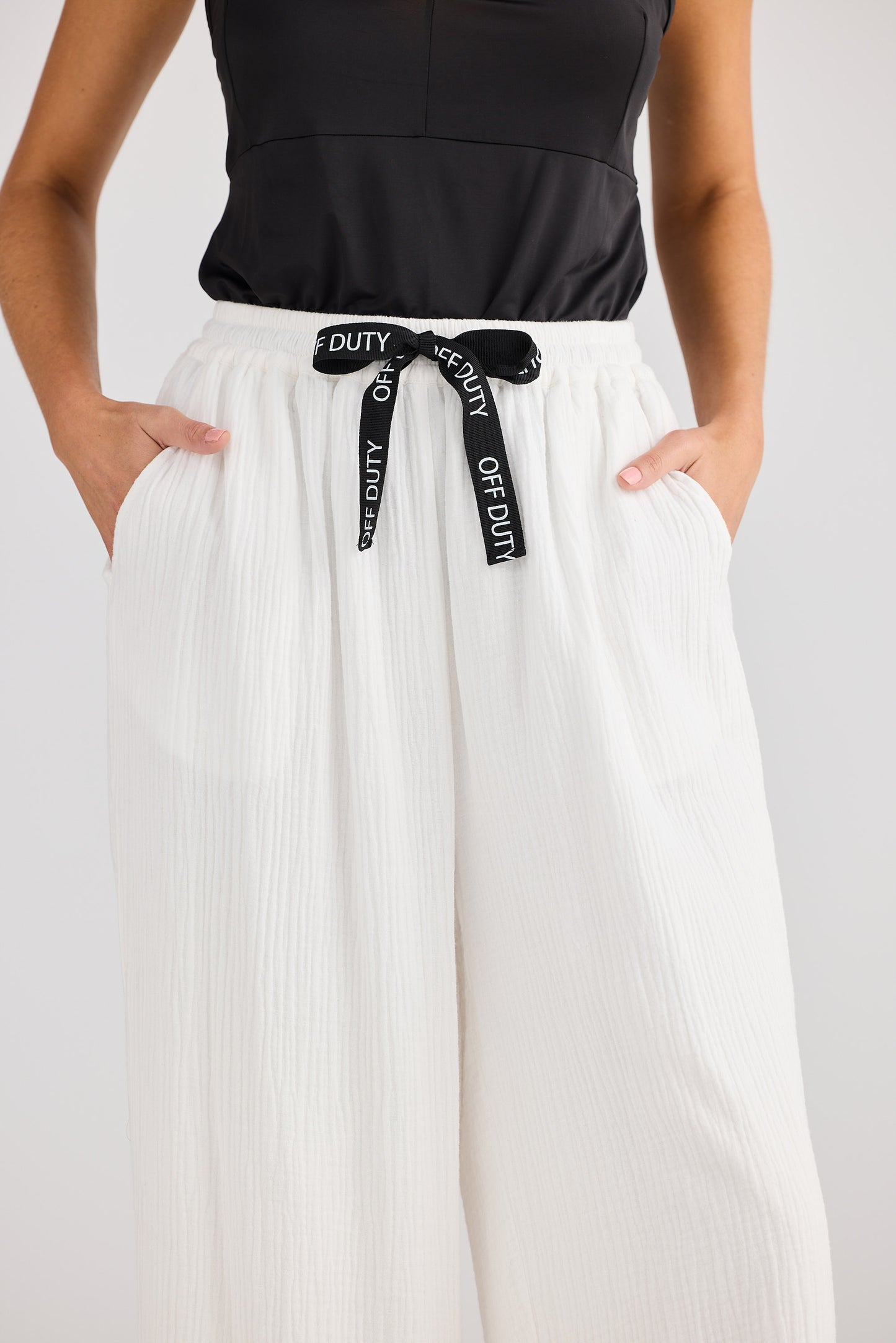 Person wearing a black top and white pants with a 'Duty' belt on a light gray background