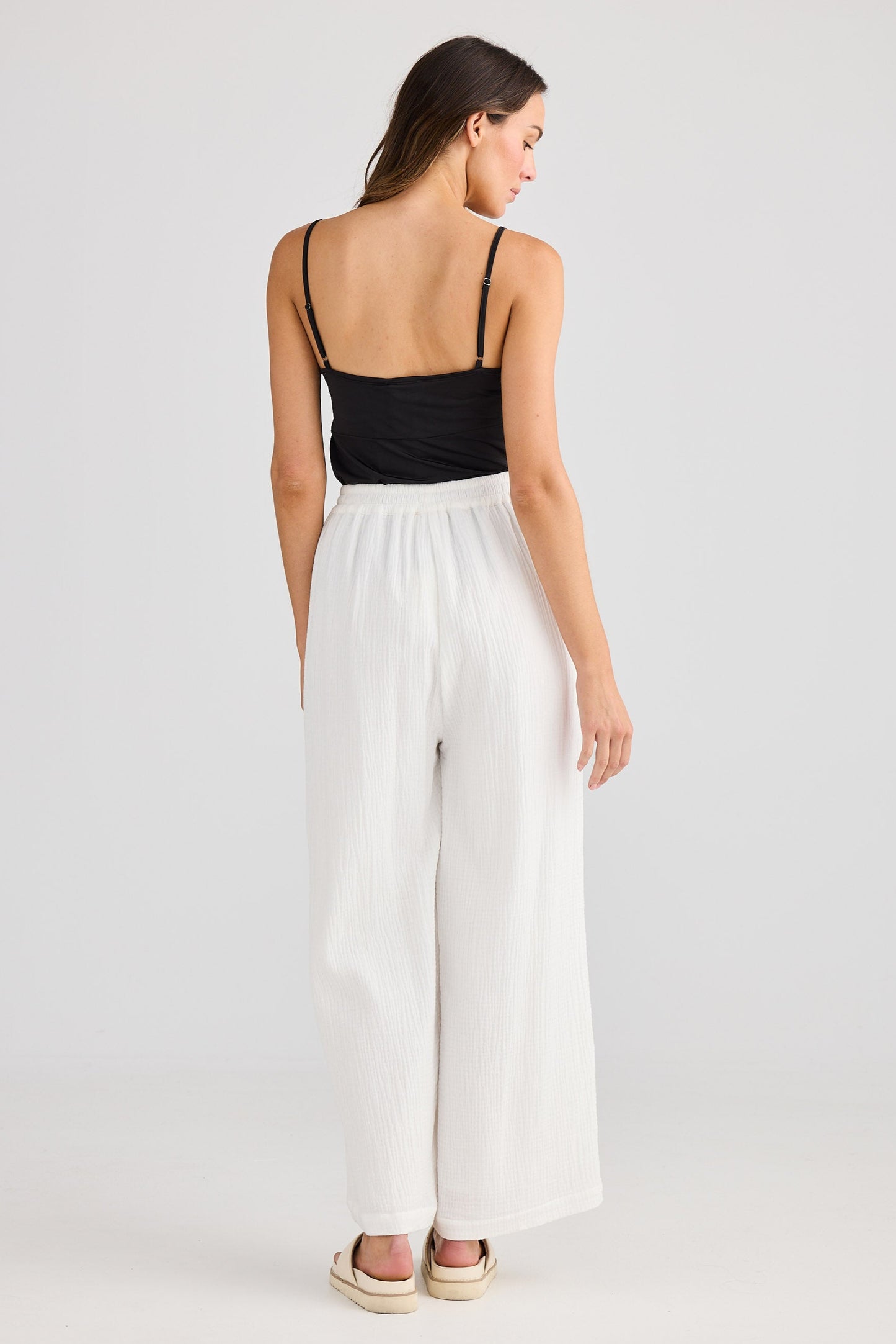Woman wearing a black top and white pants on a plain background