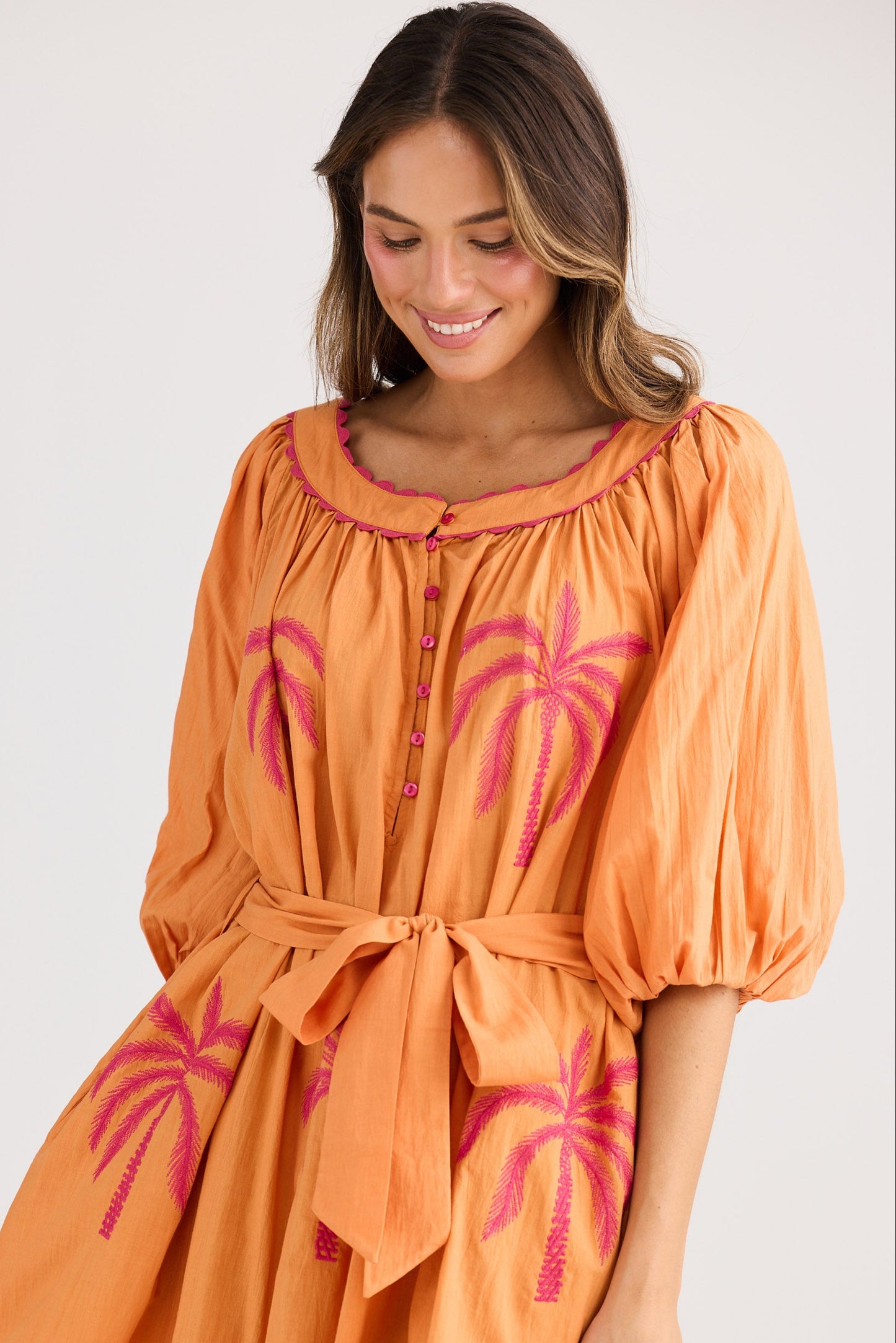 Woman wearing an orange dress with pink palm tree patterns on a white background