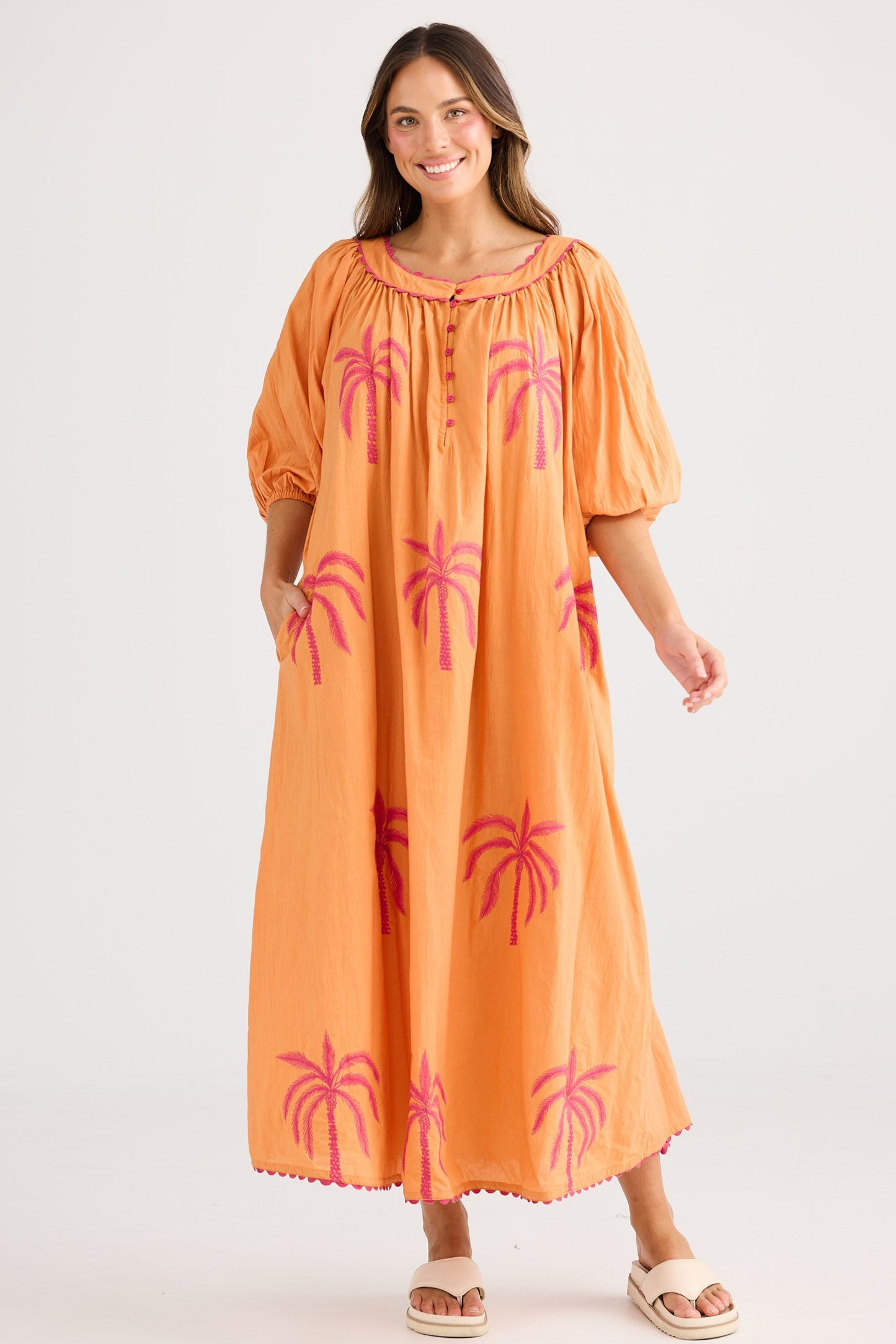Woman wearing an orange dress with pink palm tree patterns on a white background