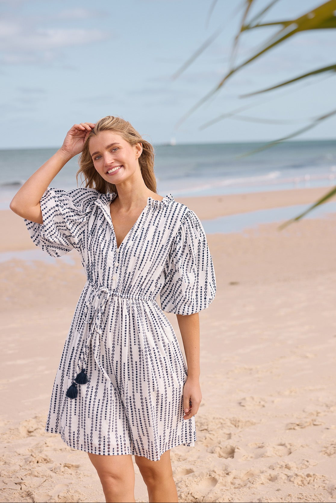 Woman in a patterened dress standing on a beach with ocean and sky in the background