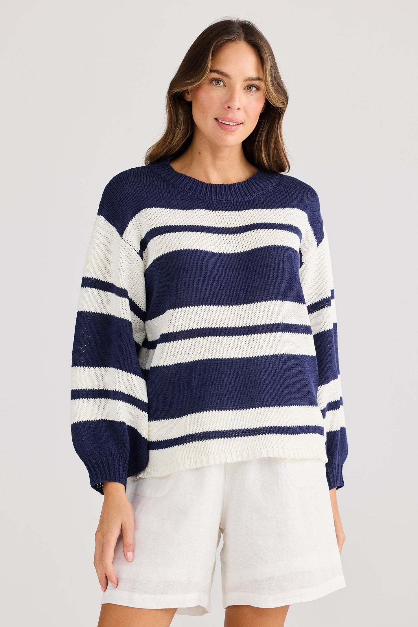 Woman wearing a navy and white striped sweater with white shorts on a light gray background