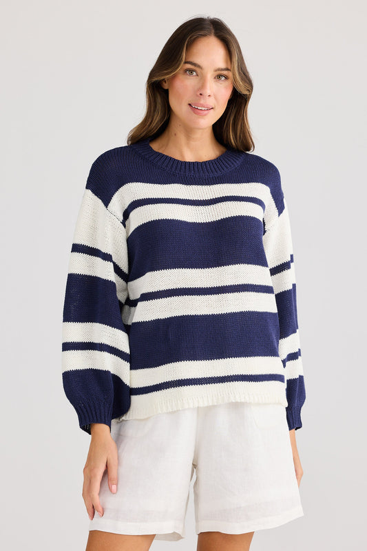 Woman wearing a navy and white striped sweater with white shorts on a light gray background