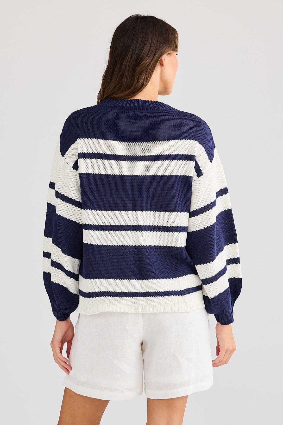 Person wearing a navy and white striped sweater with white shorts on a light gray background