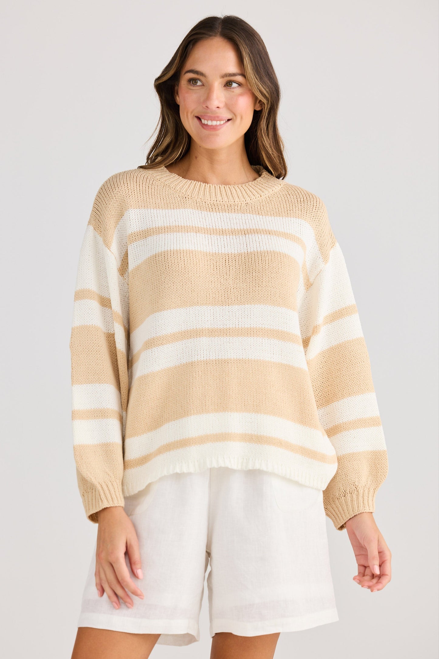 Woman wearing a beige and white striped sweater with white shorts on a plain background