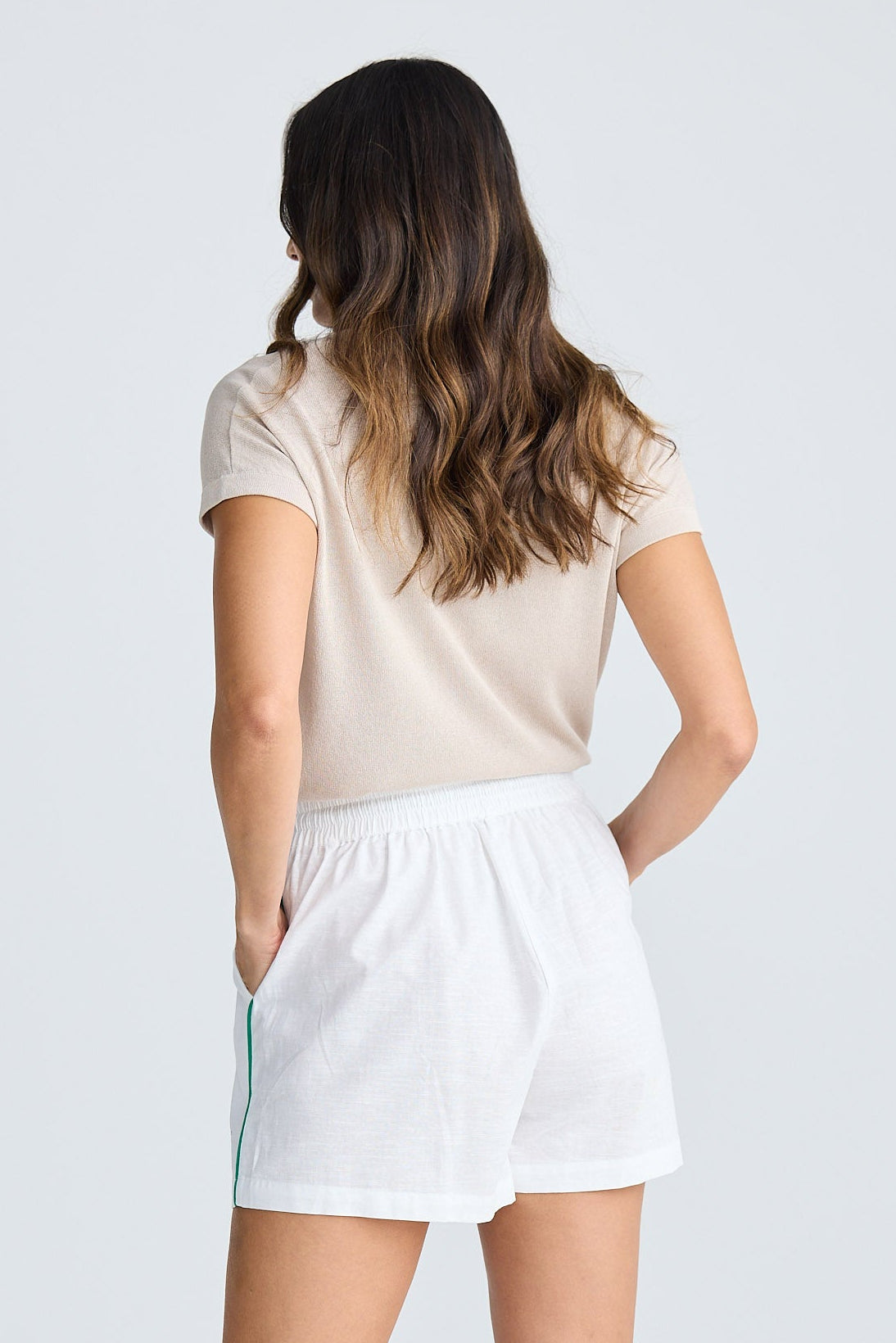 Woman wearing a beige t-shirt and white shorts on a plain background