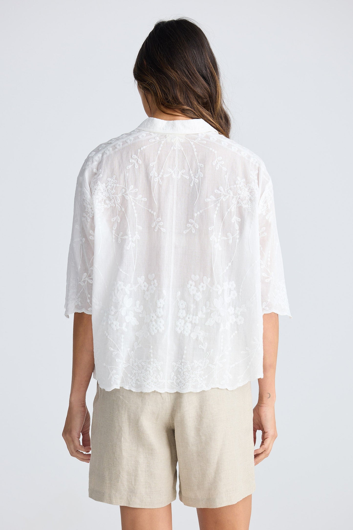 Person wearing a white lace top and beige shorts on a plain background