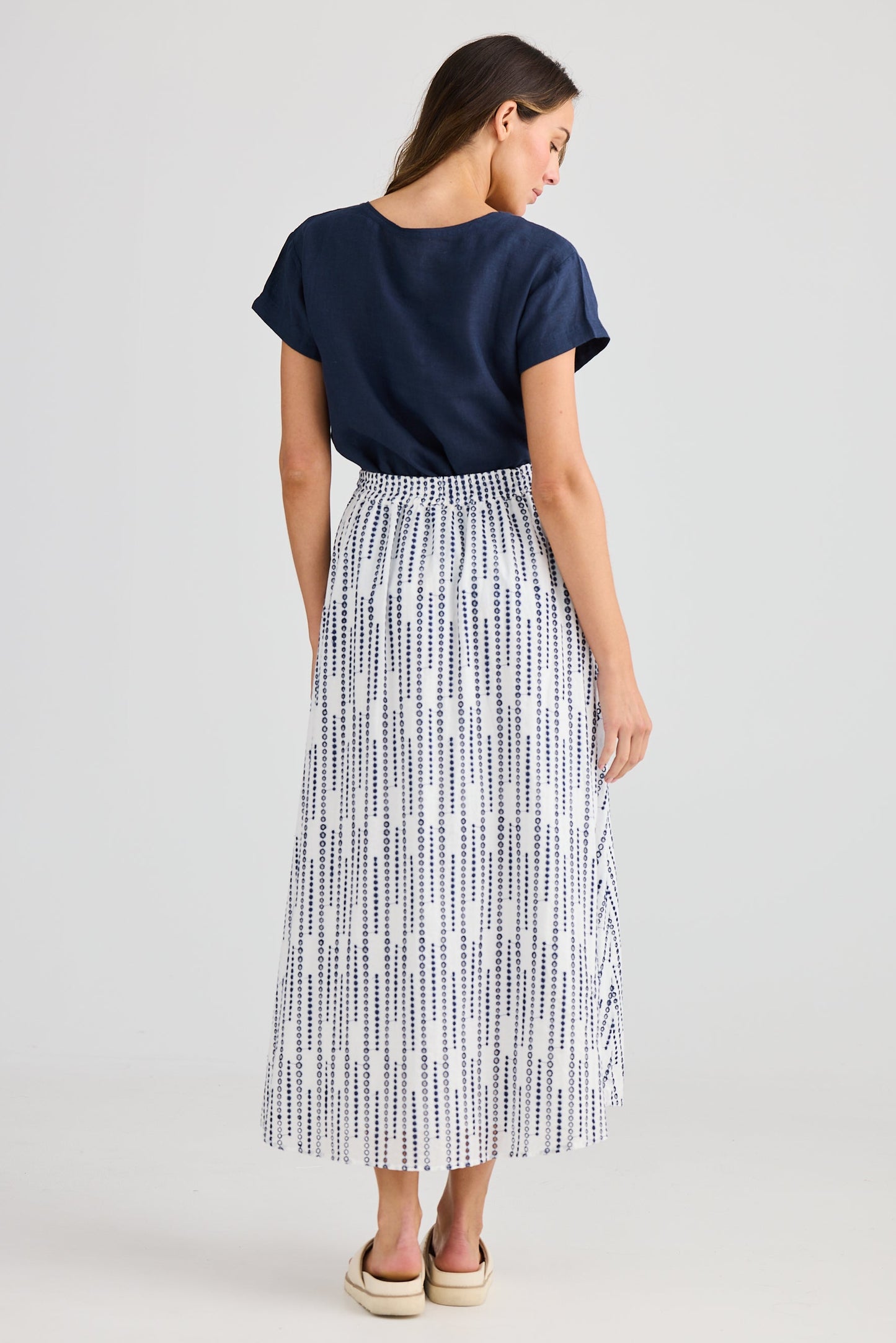 Woman wearing a navy t-shirt and patterned skirt on a white background