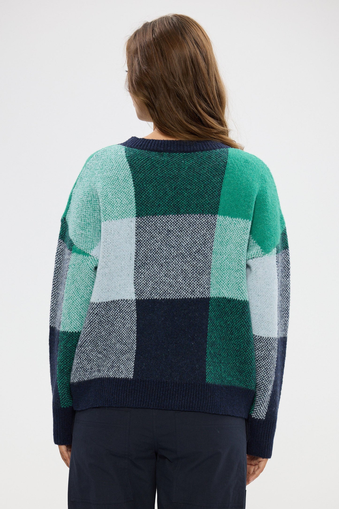 Person wearing a checkered sweater with green, blue, and gray pattern on a white background