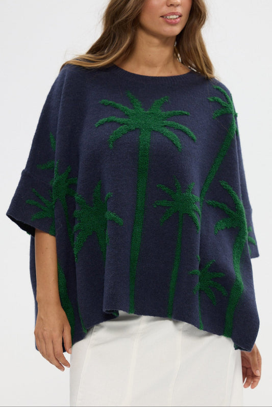 Woman wearing a navy blue poncho with green palm tree patterns on a white background