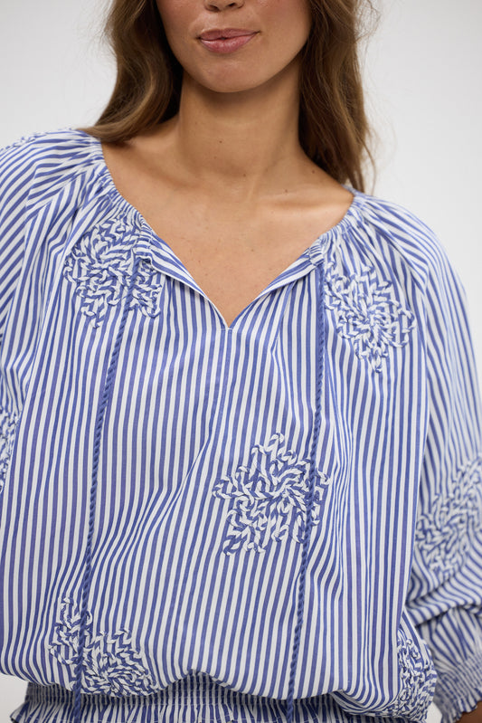 Woman wearing a blue and white striped blouse with floral patterns.