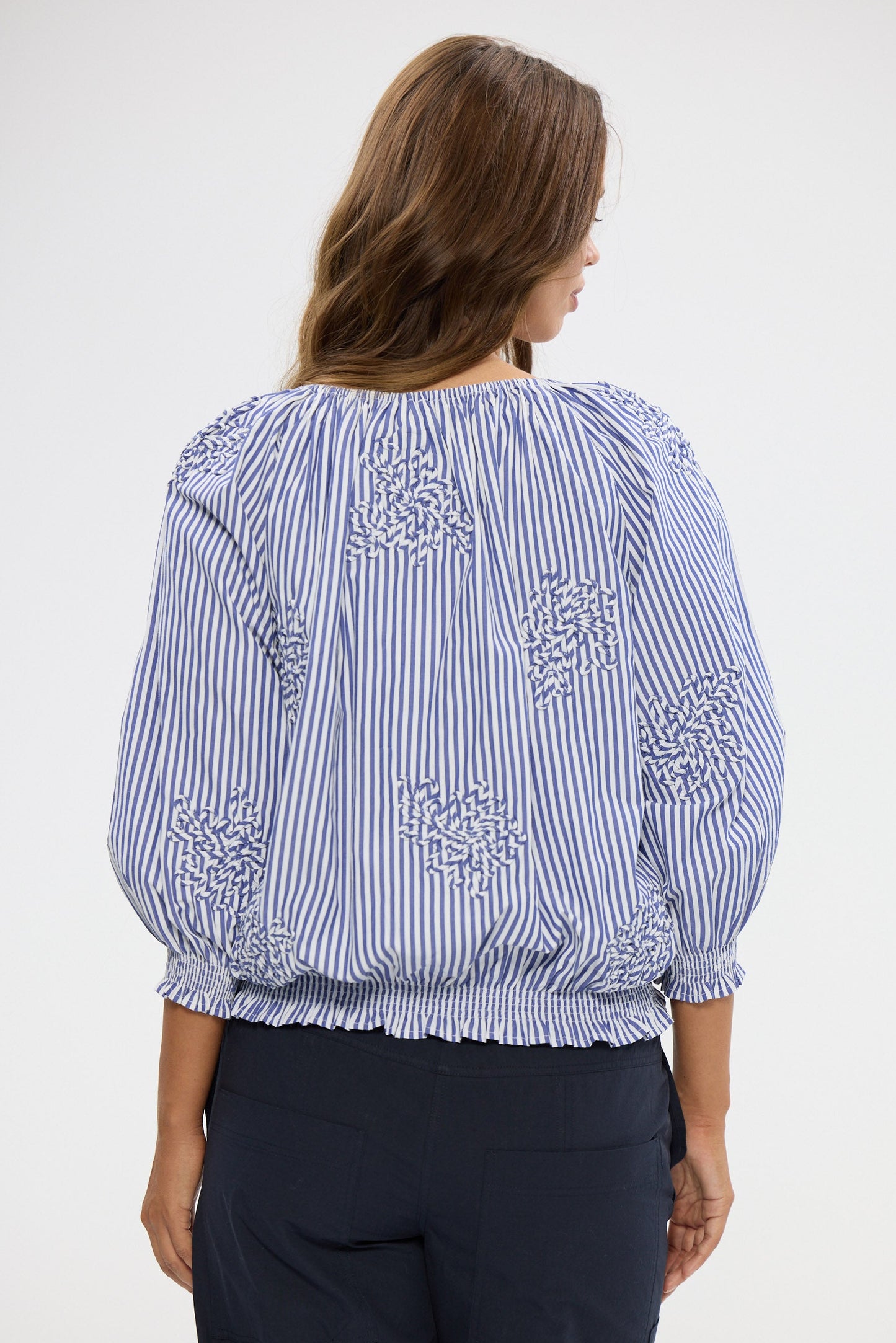 Woman wearing a blue and white striped blouse with floral embroidery on a white background