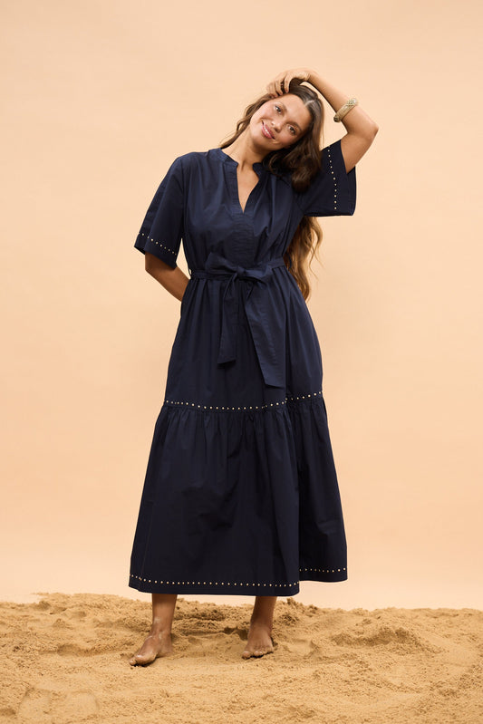 Woman in a navy dress standing on sand with a beige background