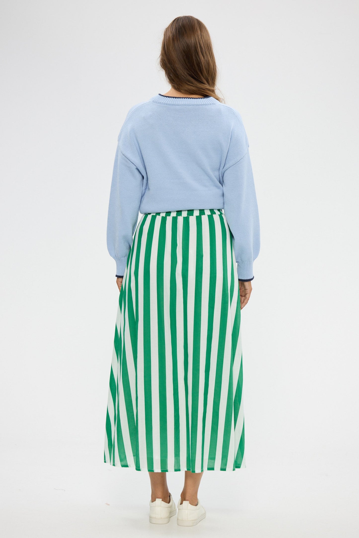 Woman wearing a light blue sweater and green and white striped skirt on a white background