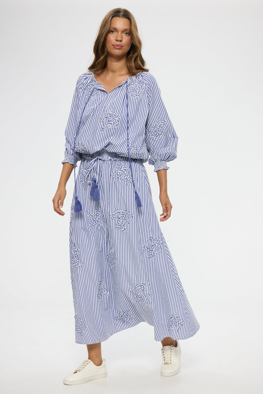 Woman wearing a blue and white striped top and skirt with embroidery on a white background