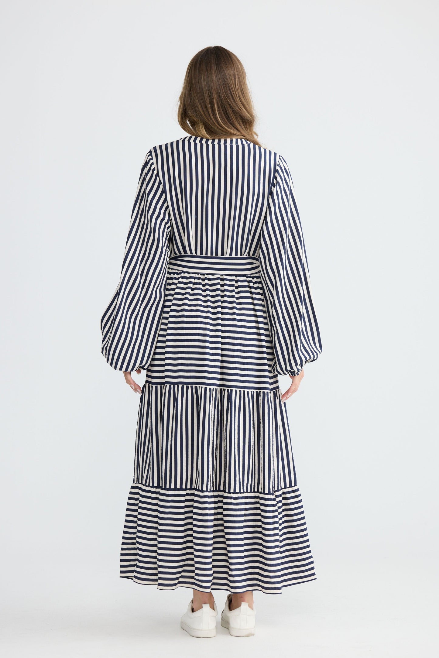 Model wearing Marla Dress Navy and White Stripe with balloon sleeves and waist tie, studio detail view on white background