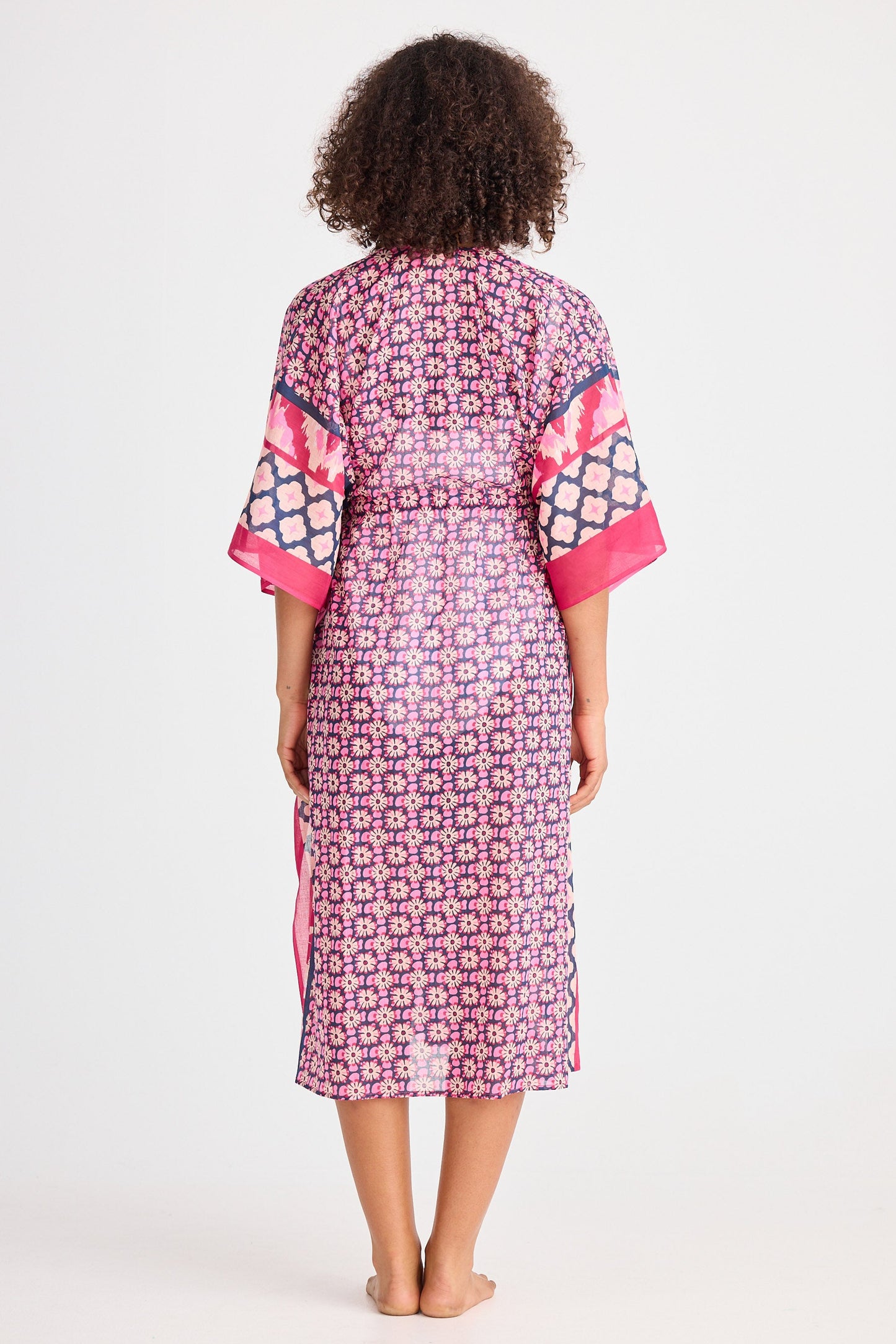 Woman wearing a patterned dress with pink accents on a white background