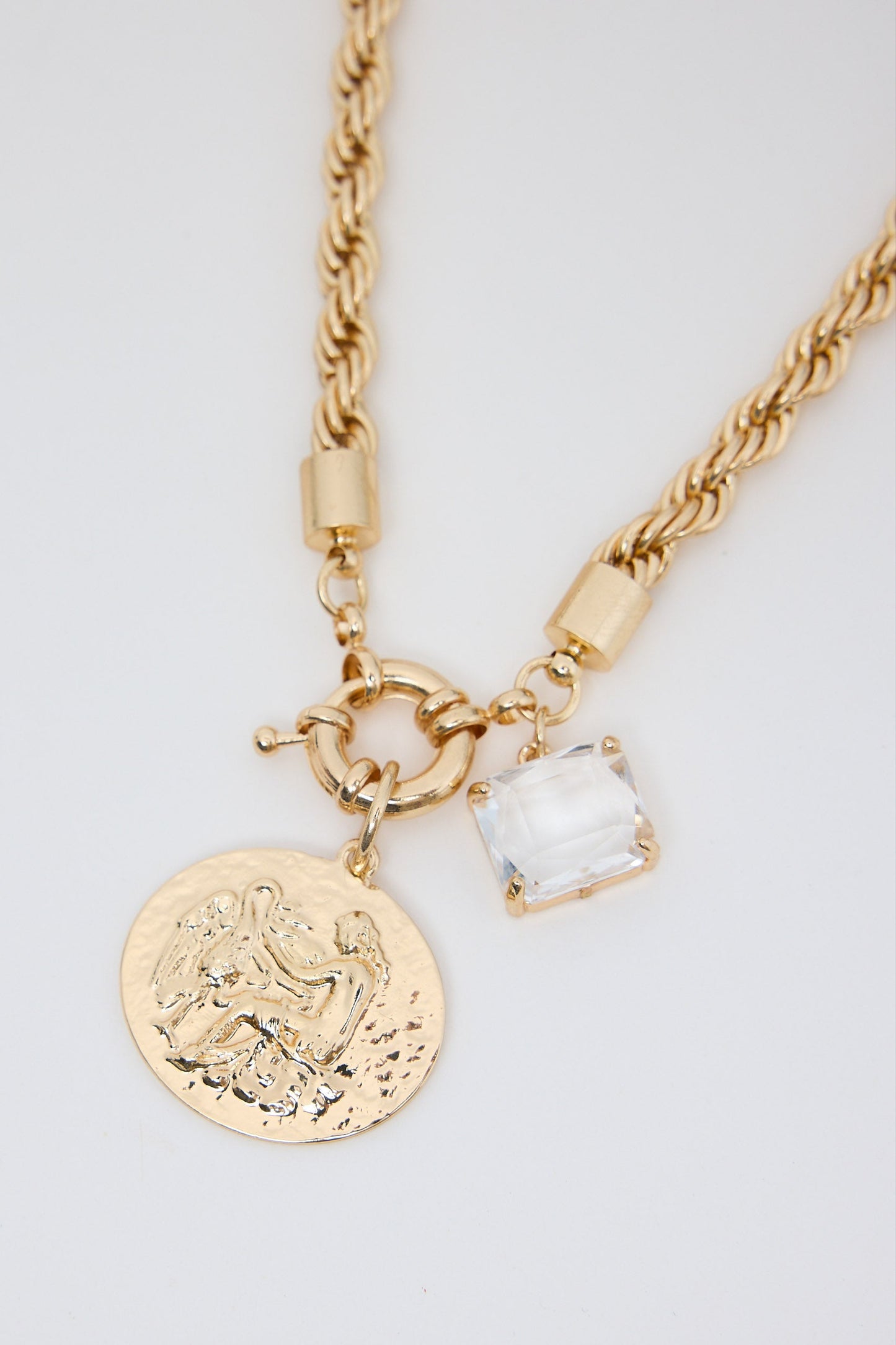 Gold necklace with a coin charm and clear pendant on a light gray background