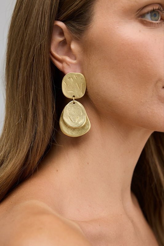 Gold earrings worn by a person with a neutral background