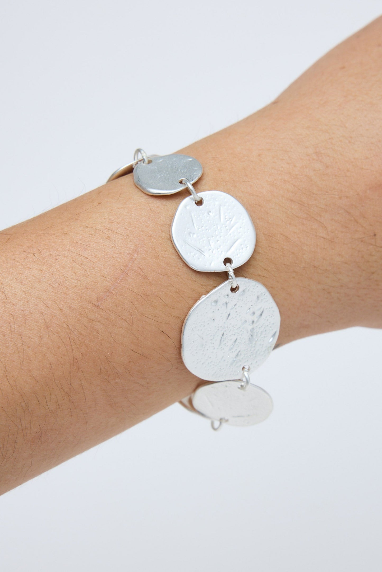 Silver bracelet with round pendants on a wrist against a white background