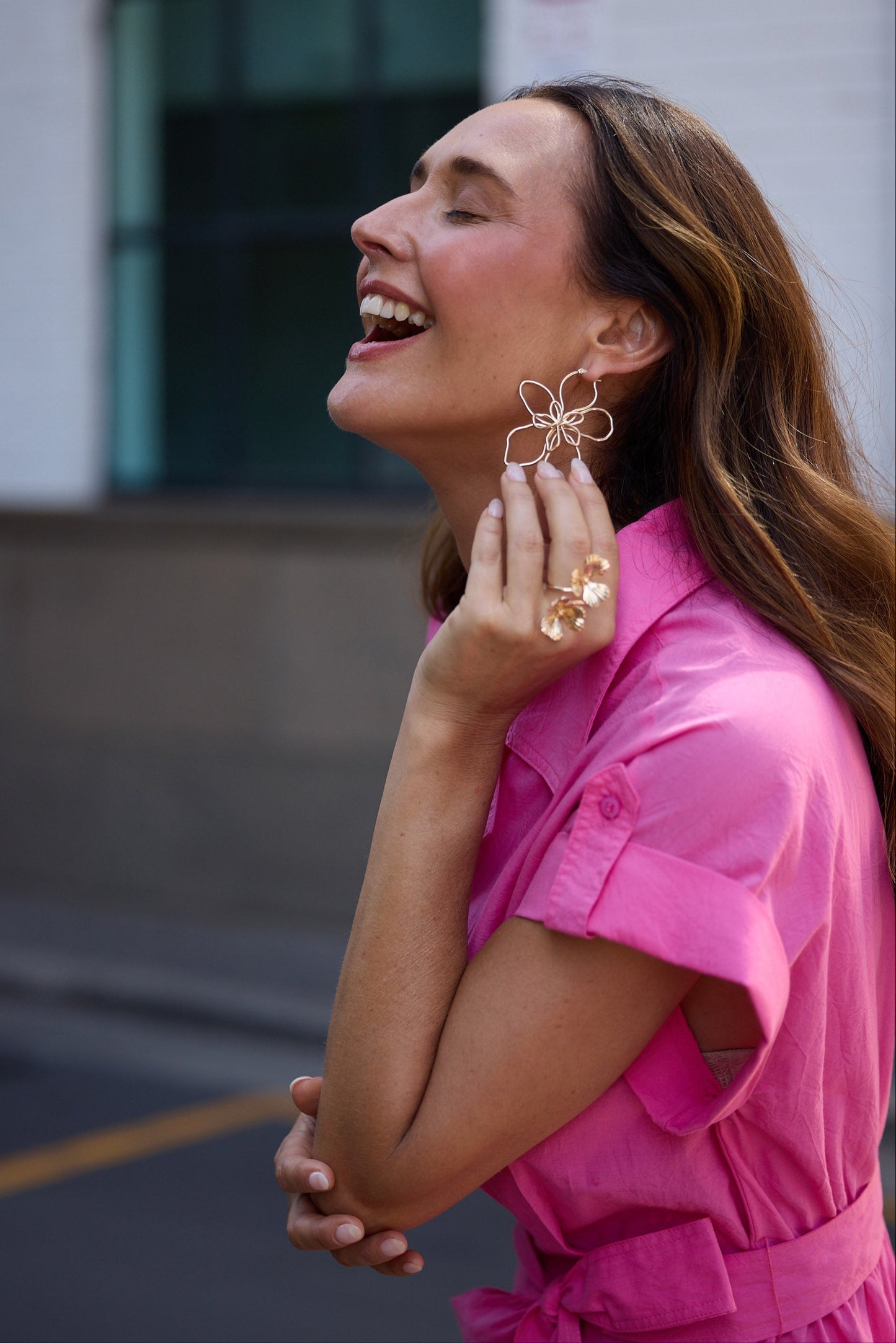 Woman in a pink dress wearing gold earrings and rings outdoors.