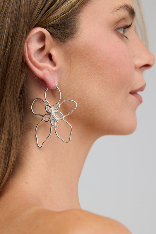 Woman wearing a silver floral earring against a plain background