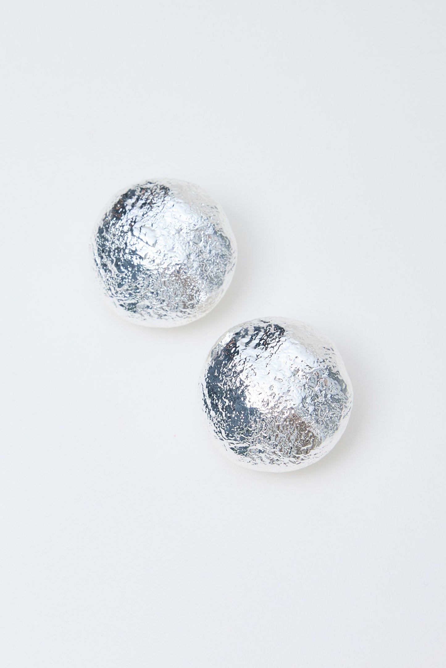 Pair of silver textured round earrings on a light gray background