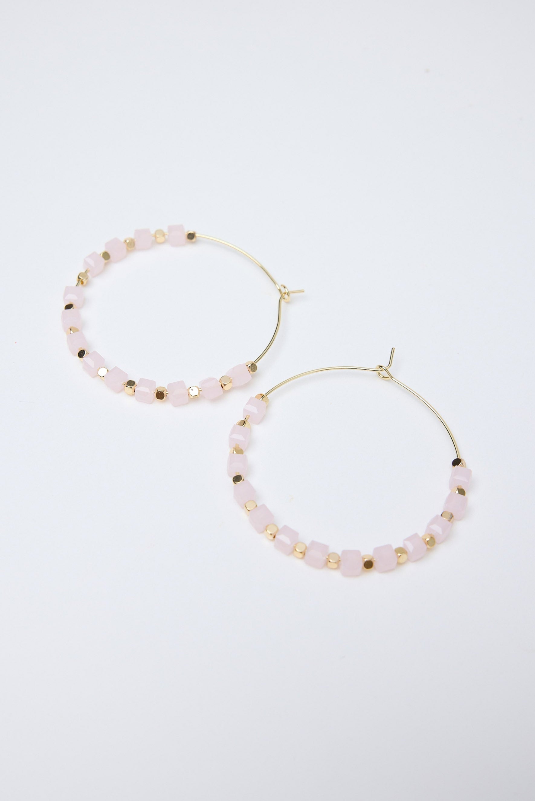 Pair of gold hoop earrings with small light pink beads on a white background