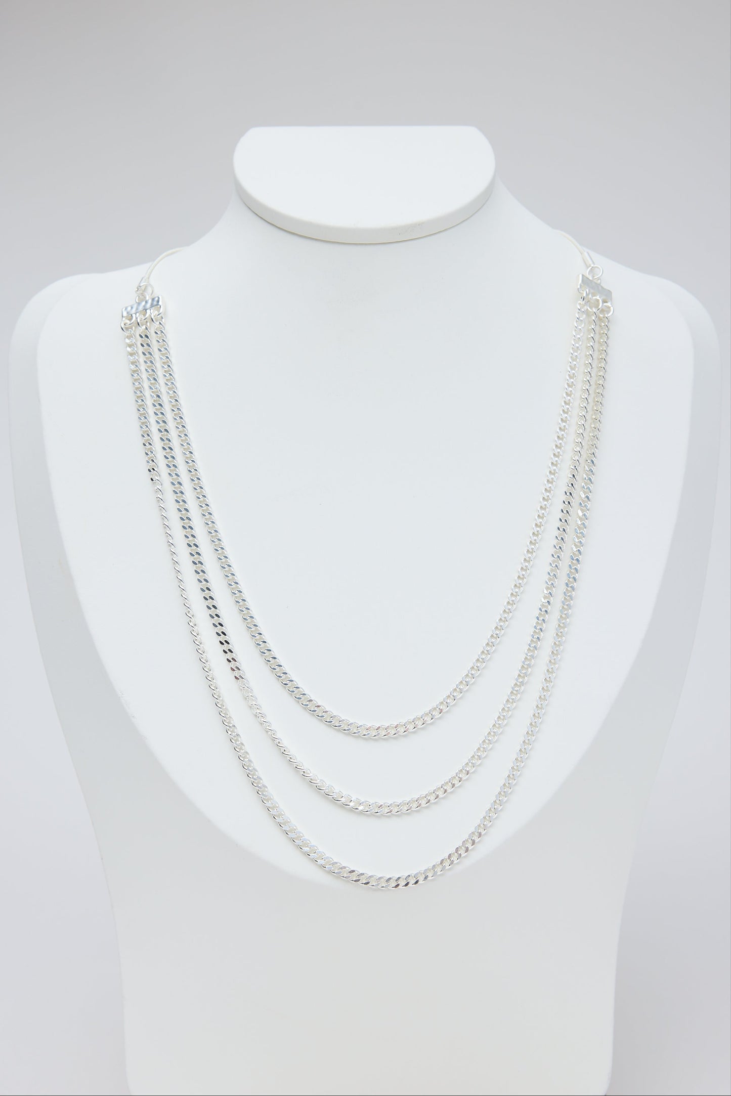 Set of silver necklaces on a mannequin bust against a light gray background