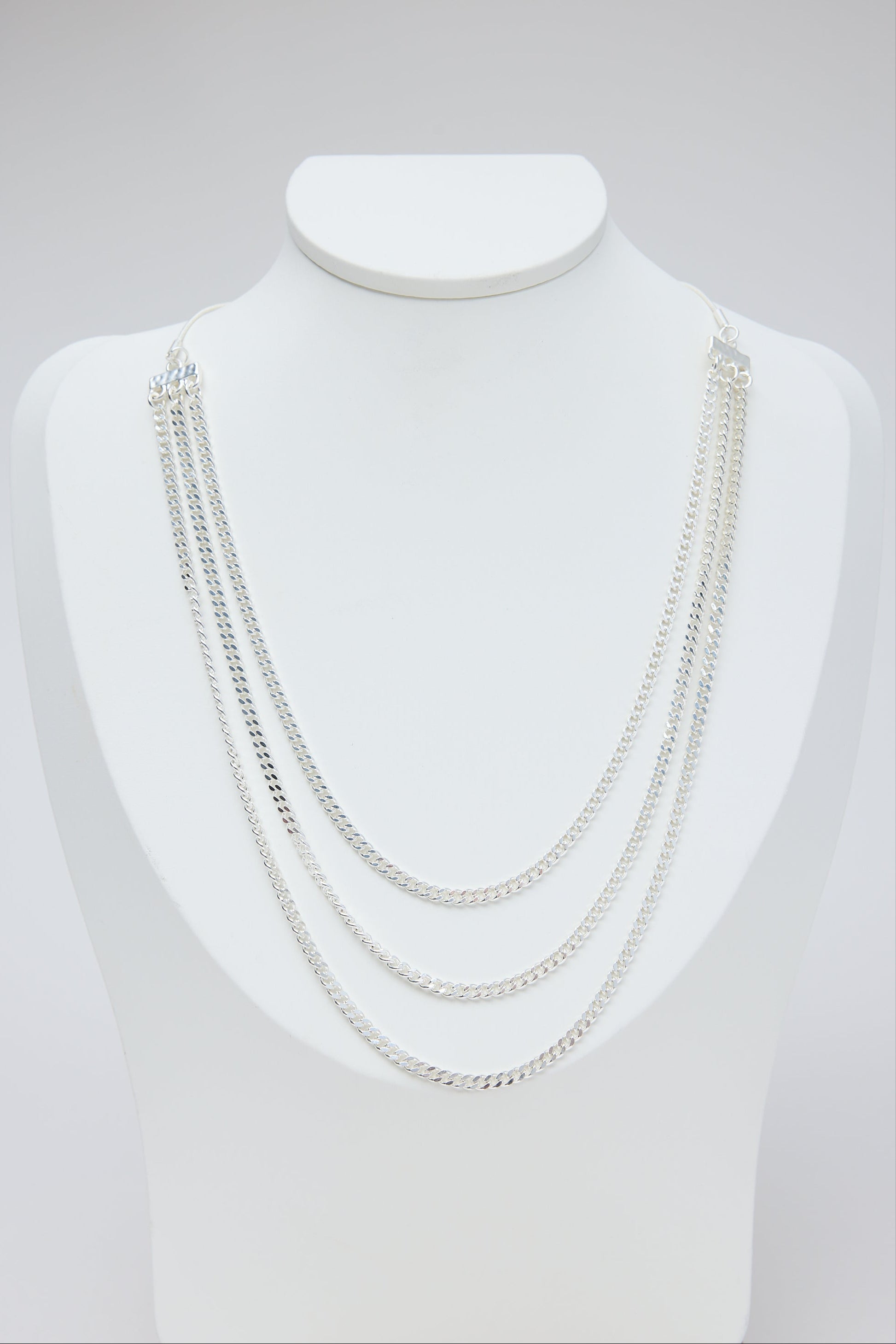 Set of silver necklaces on a mannequin bust against a light gray background