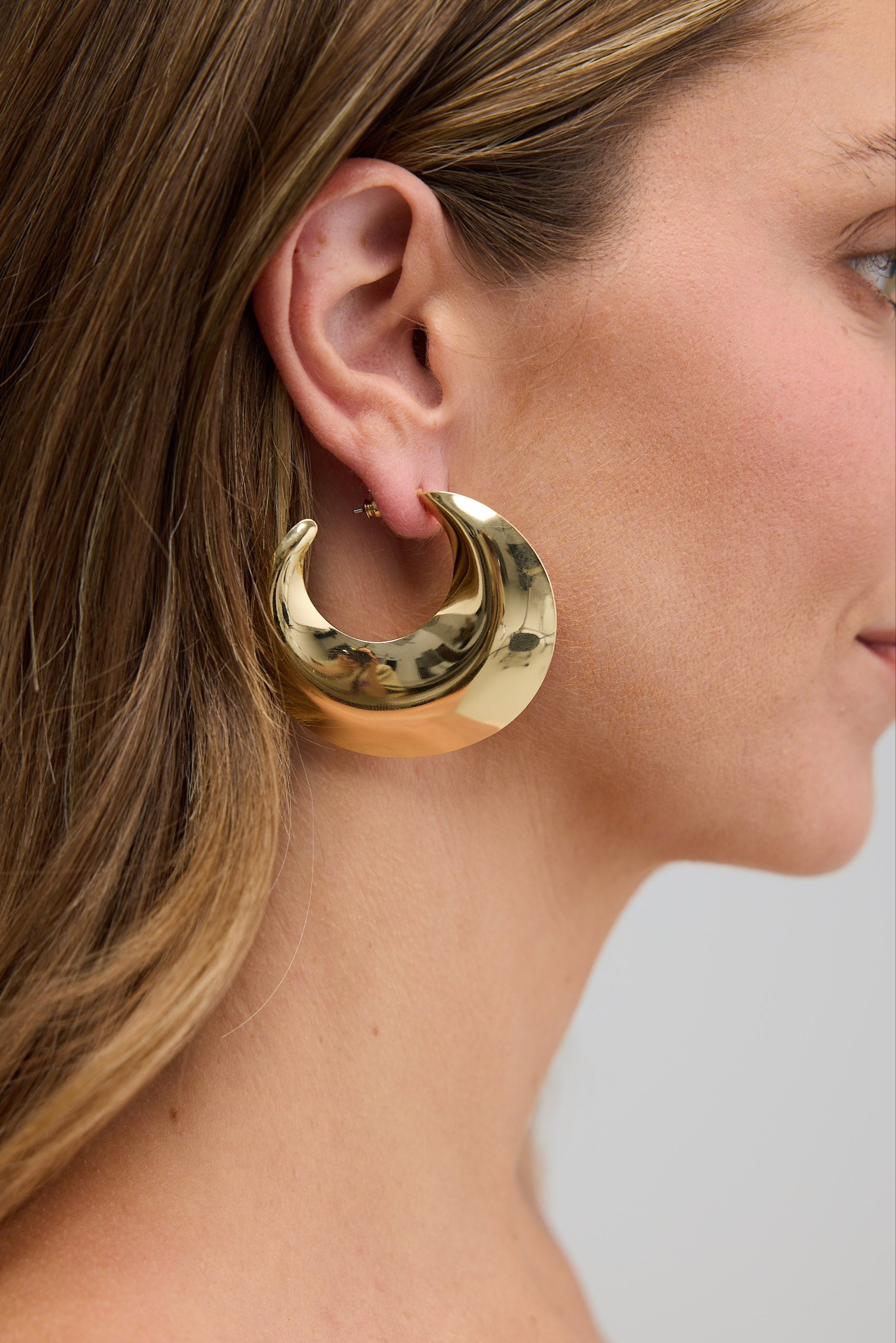 Gold hoop earring worn by a person with a neutral background