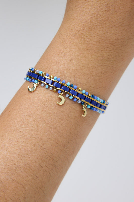 Bracelet with blue beads and gold accents on a wrist against a light gray background