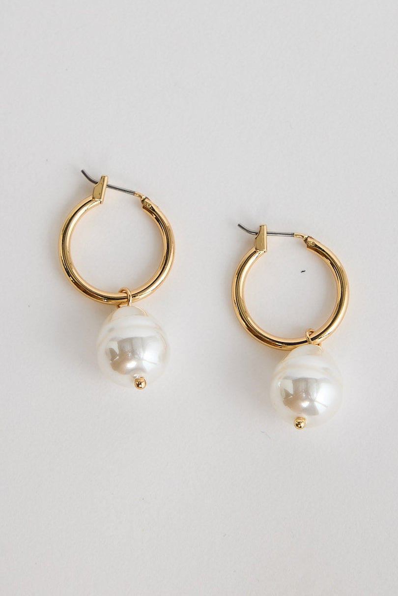 Gold hoop earrings with pearl drops on a light gray background