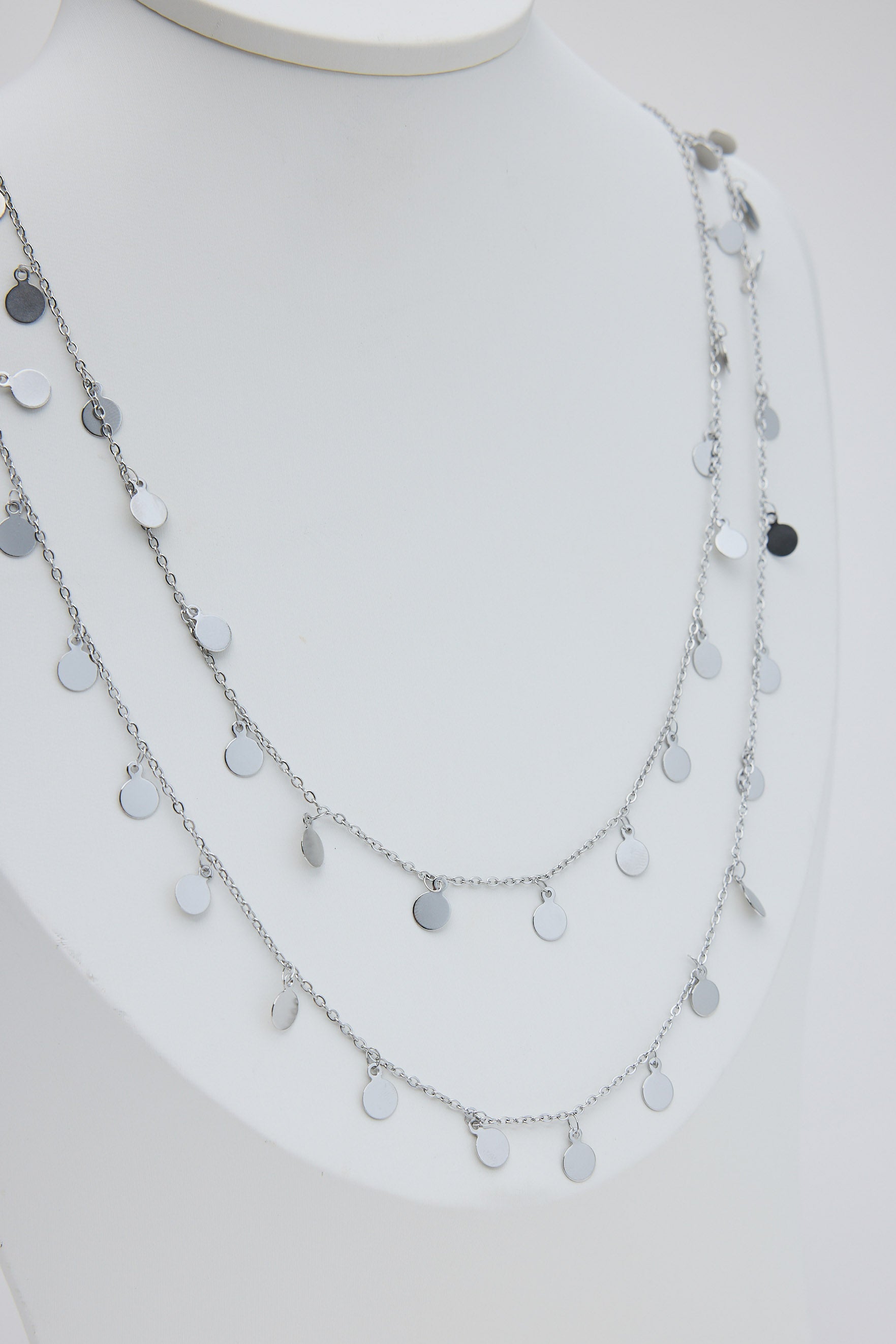 Layered silver necklace on a mannequin with a plain background