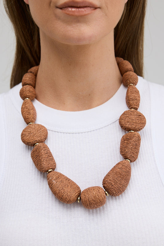 Person wearing a large brown beaded necklace on a plain background