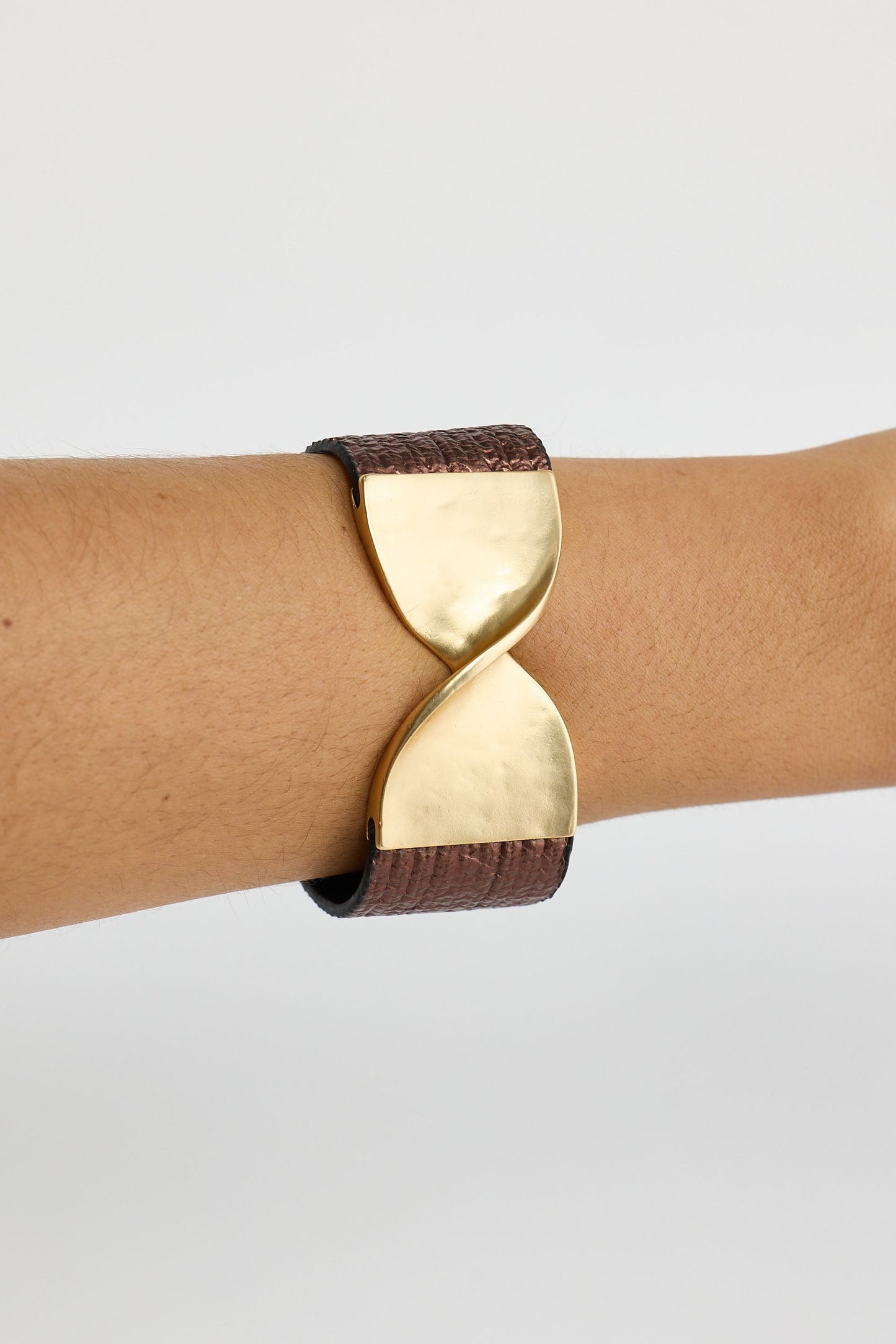 Gold and brown hourglass-shaped bracelet on a wrist against a light gray background