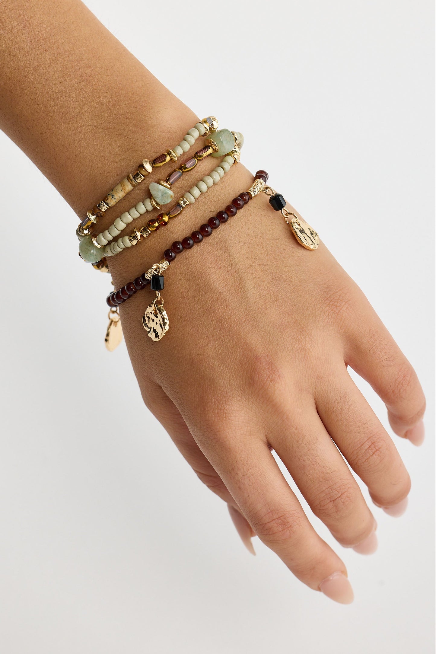 Hand wearing multiple beaded bracelets on a light background