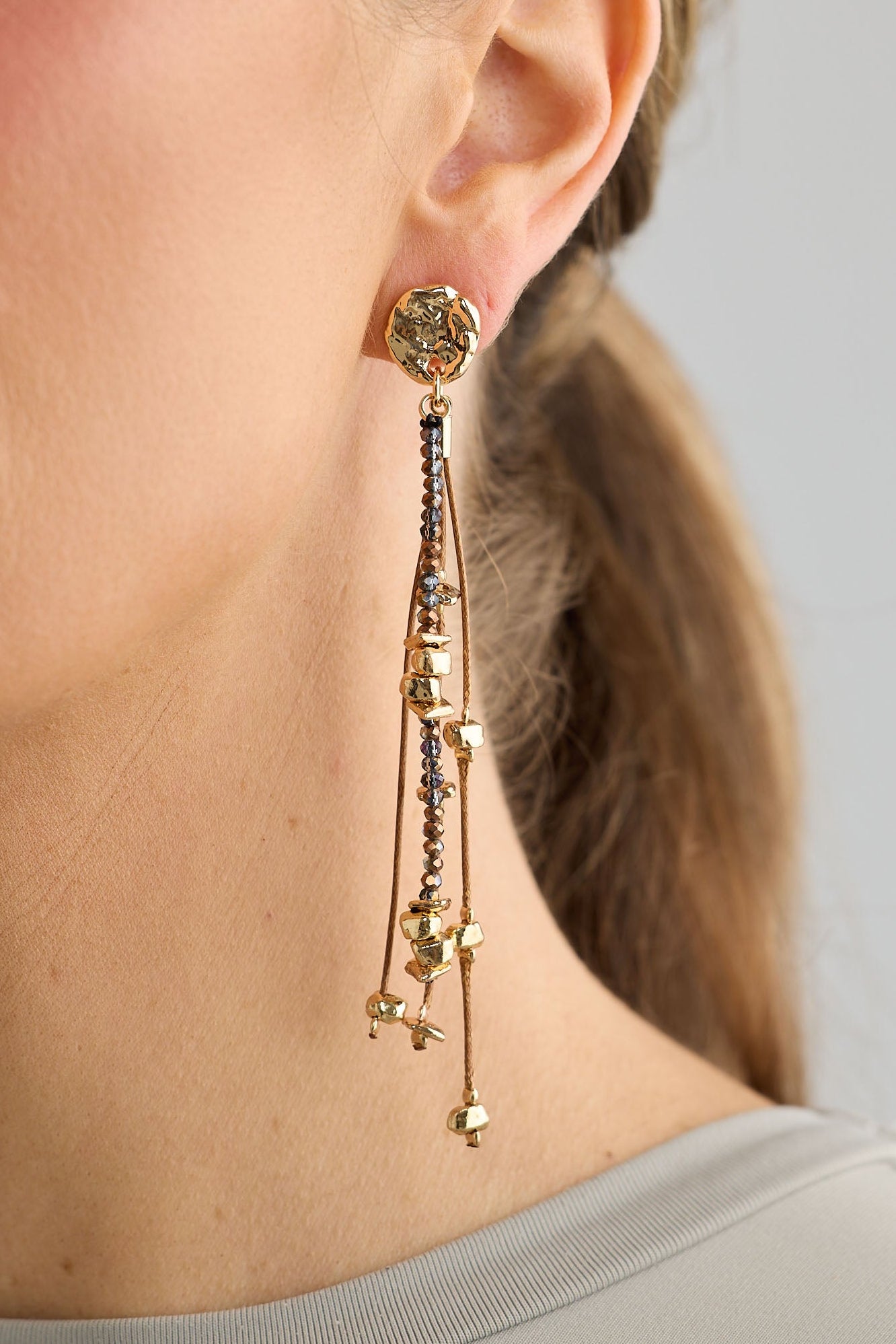 Close-up of a woman wearing gold earrings with a neutral background