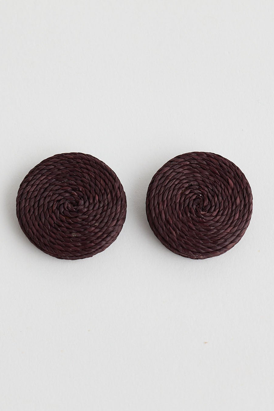 Pair of round dark brown earrings on a light gray background