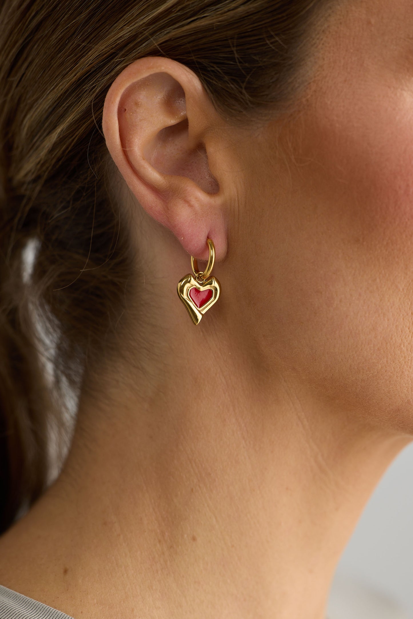 Gold heart-shaped earring with a red gemstone worn by a person.