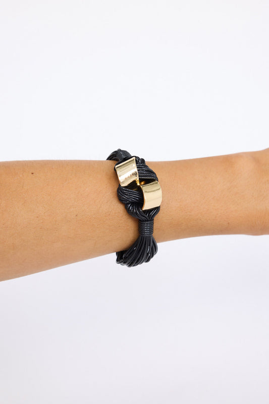 Model wearing Kazima Bracelet in black with bold knot detailing and metal accents, on-wrist view on neutral background