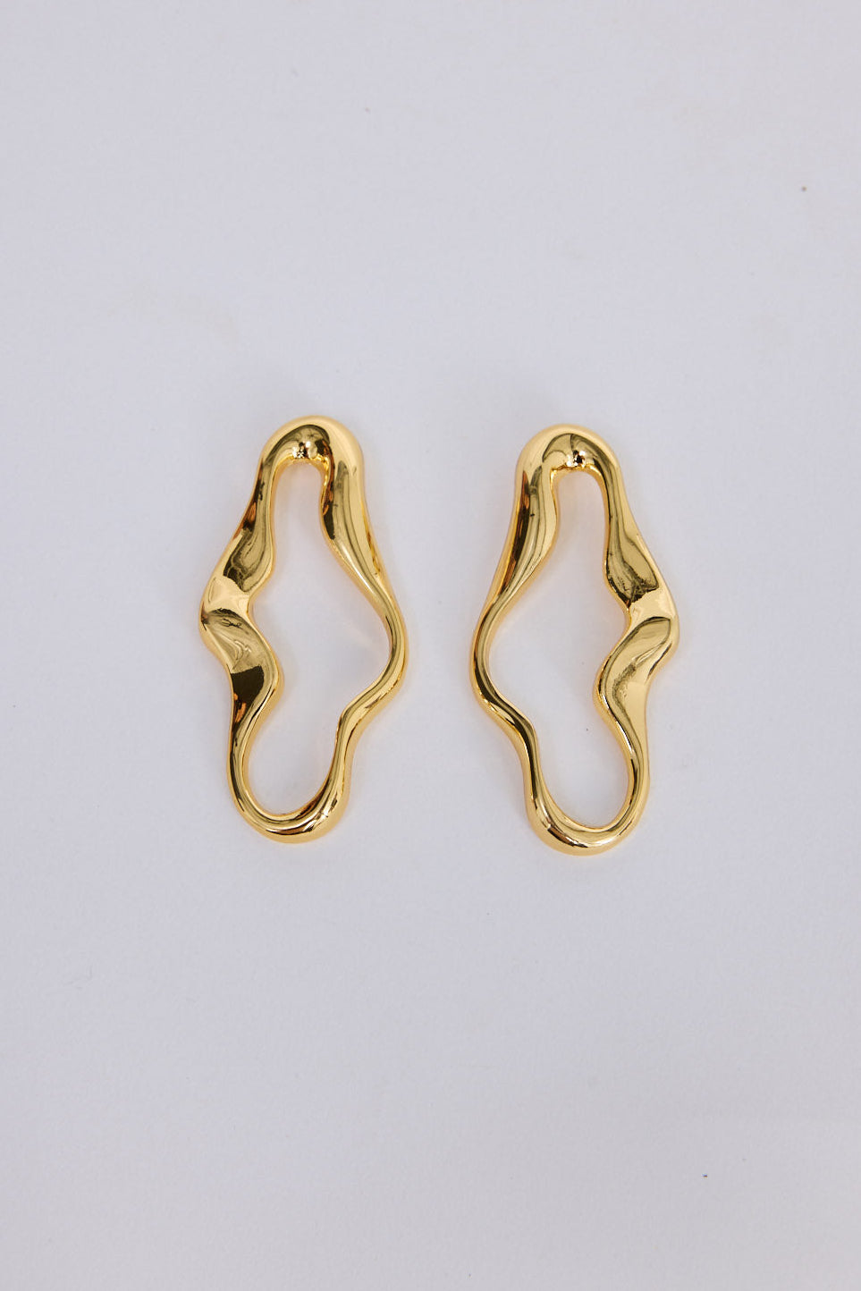 Benny Earrings in gold with a fluid sculptural silhouette, front view on white background