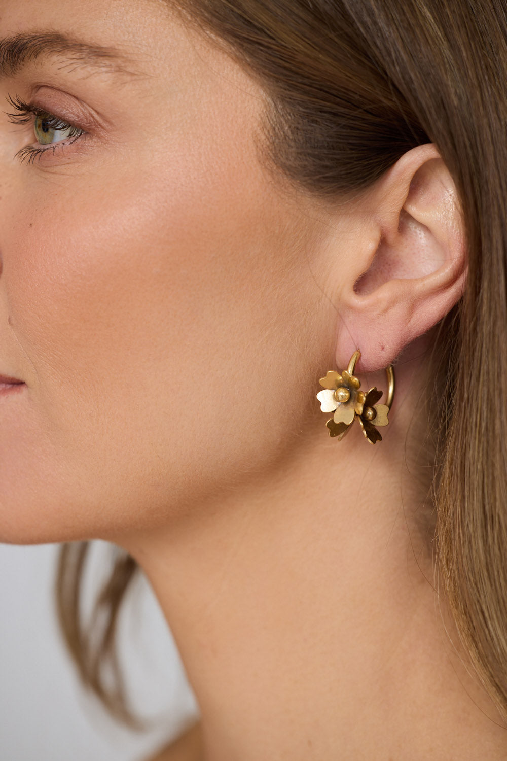 Model wearing Liucienne Earrings in gold with floral drop detailing, model close-up view on neutral background