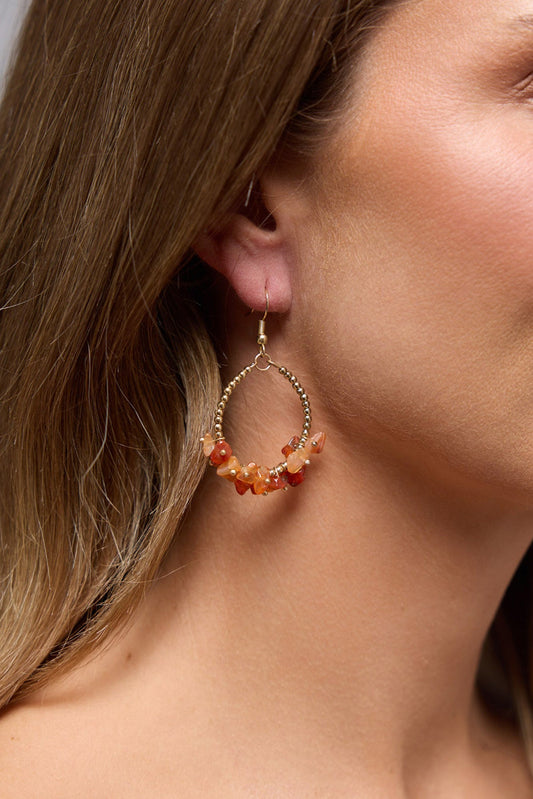 Close-up of the Yalla hoop earring worn on the ear, showing the gold beaded hoop and orange stone chip cluster against the hair