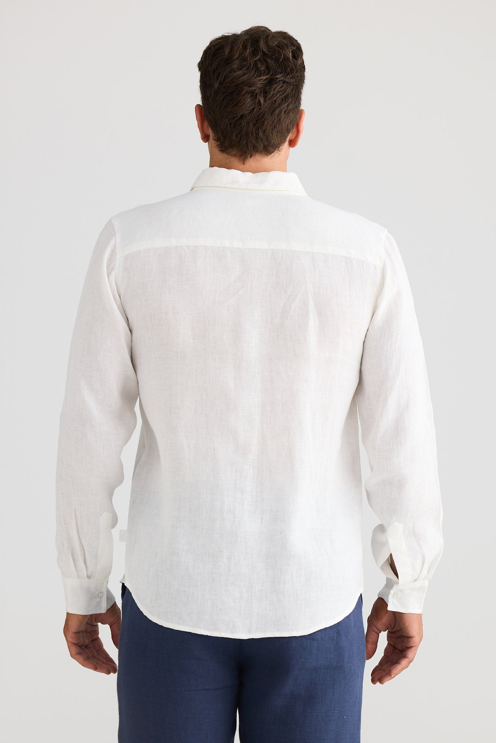 Man wearing a white shirt and blue pants on a plain background