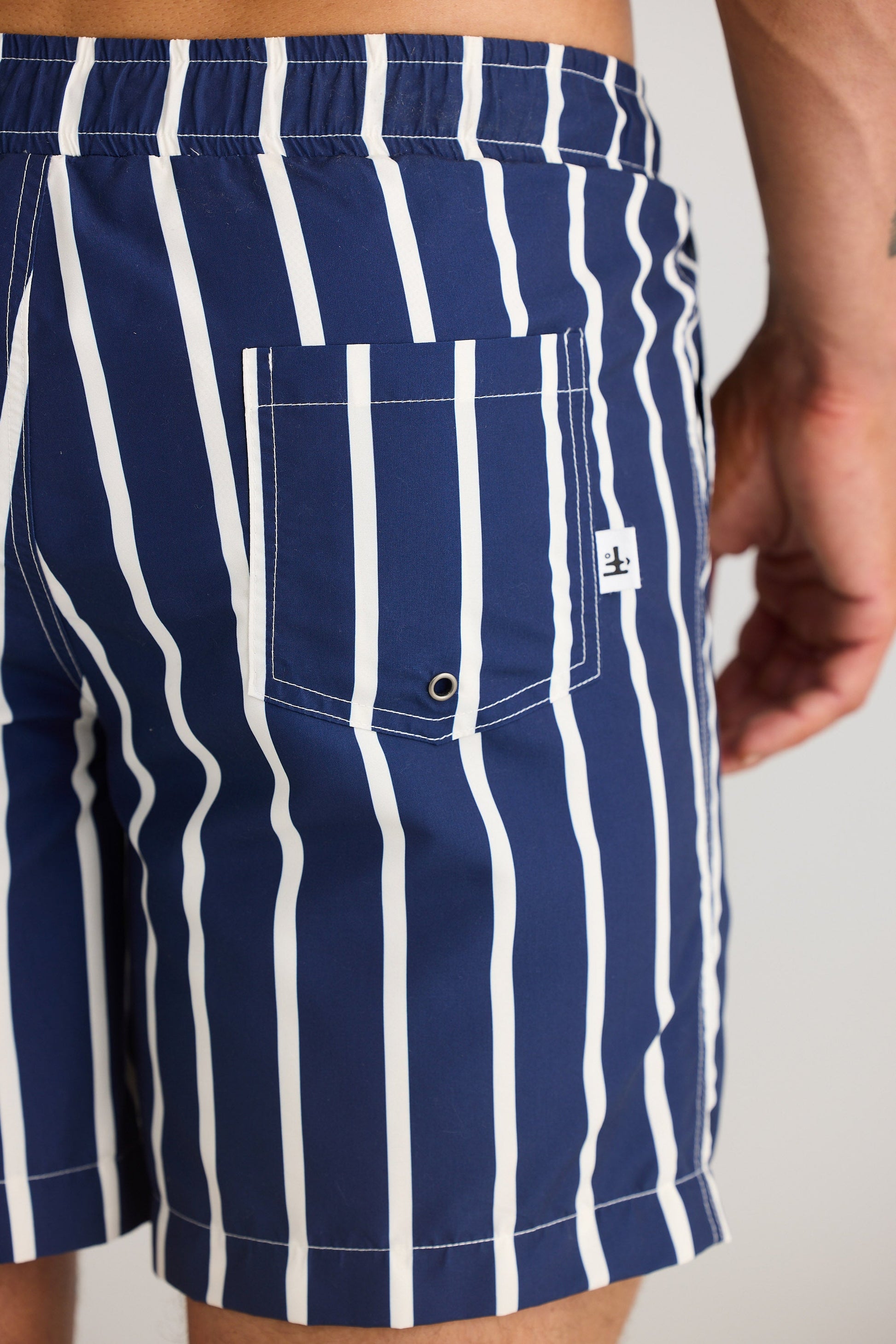Navy and white striped swim shorts with a brand logo on a neutral background