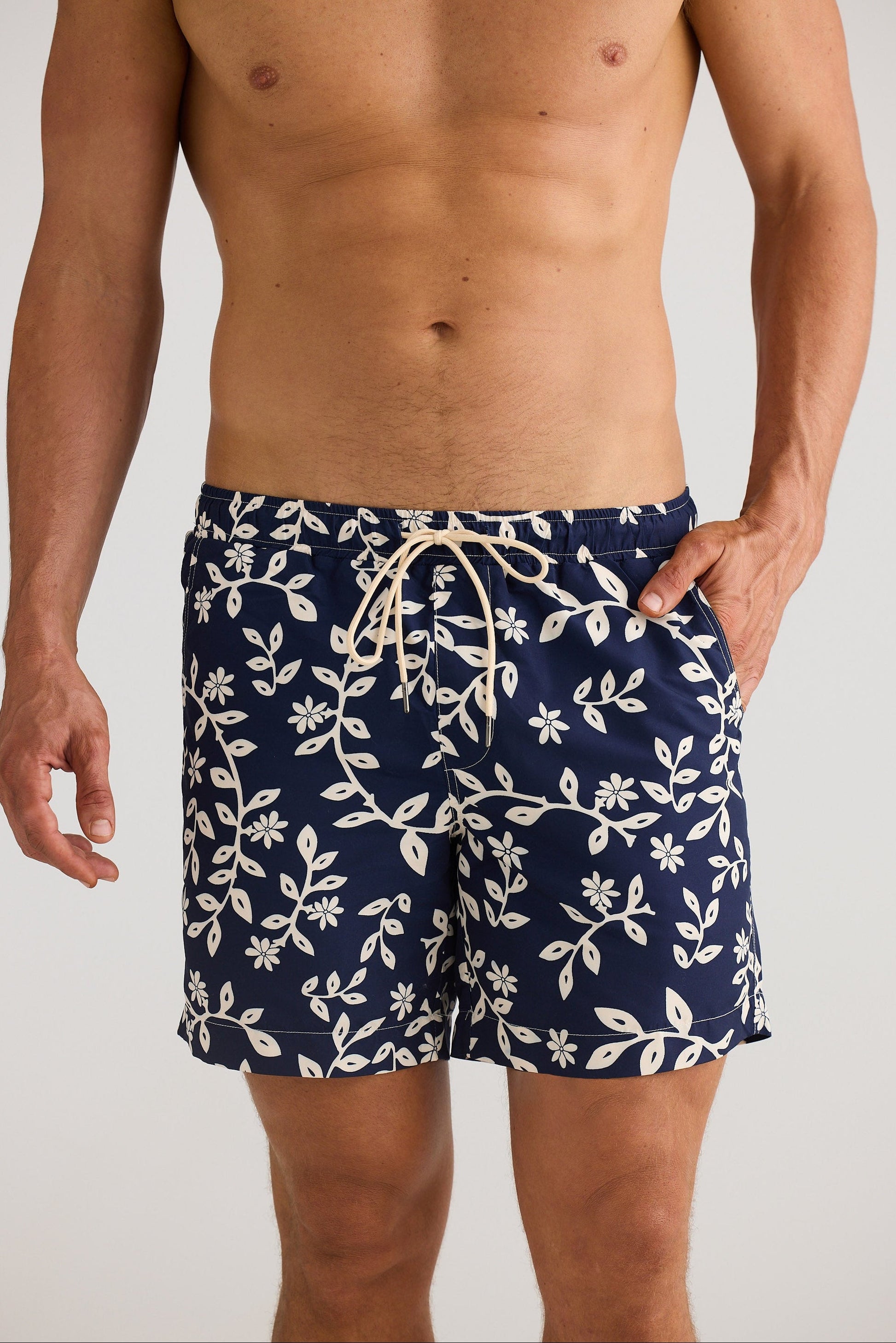 Man wearing navy blue swim shorts with white floral pattern on a plain background