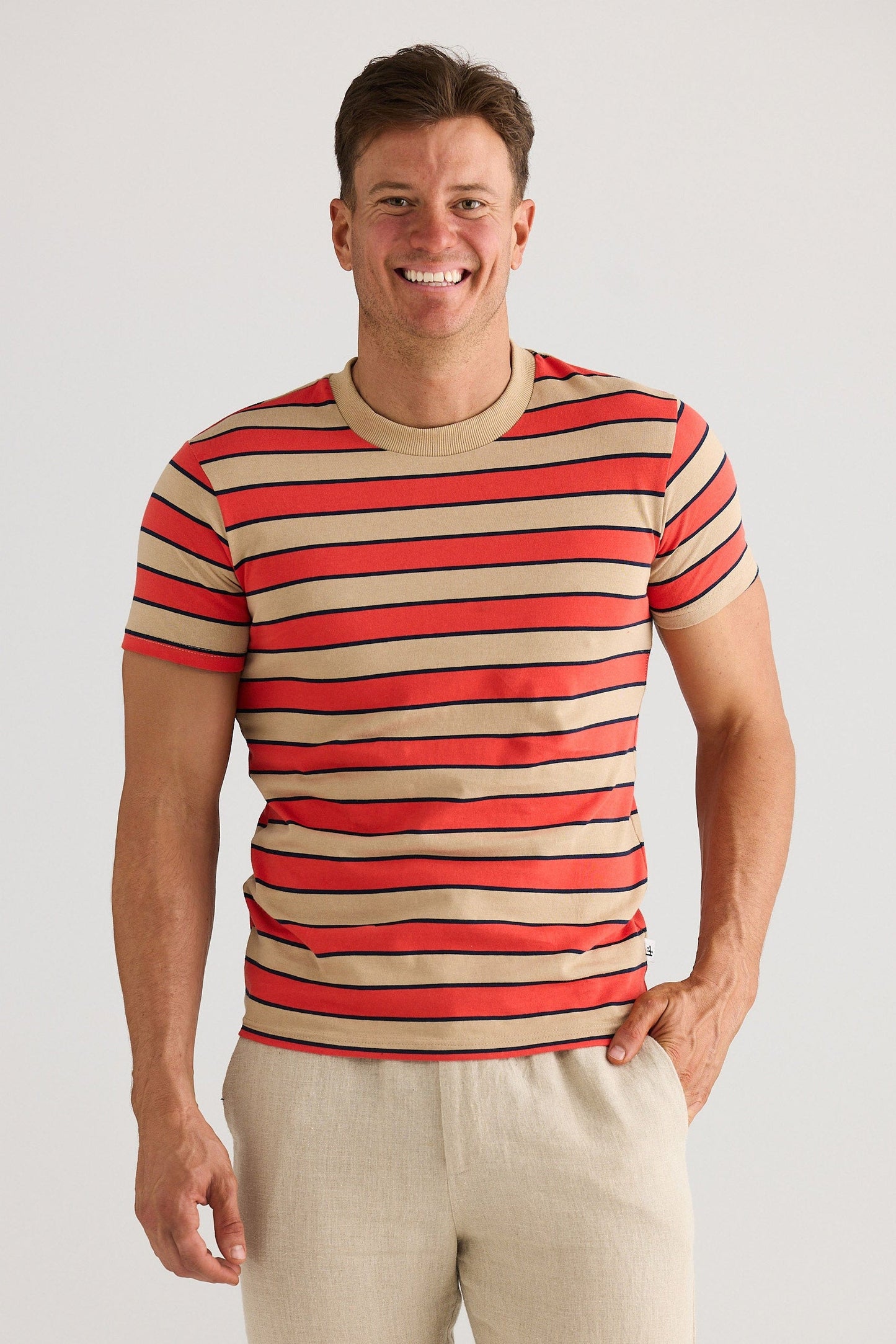 Man wearing a red and beige striped shirt with beige pants on a white background